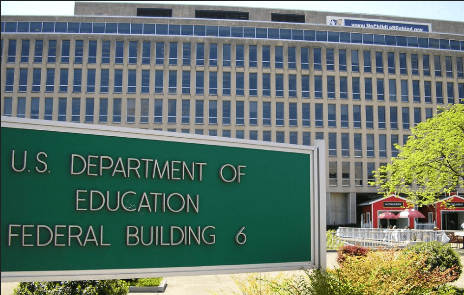 The image shows the exterior of the Department of Education Headquarters in Washington DC with a green sign indicating the name of the department.