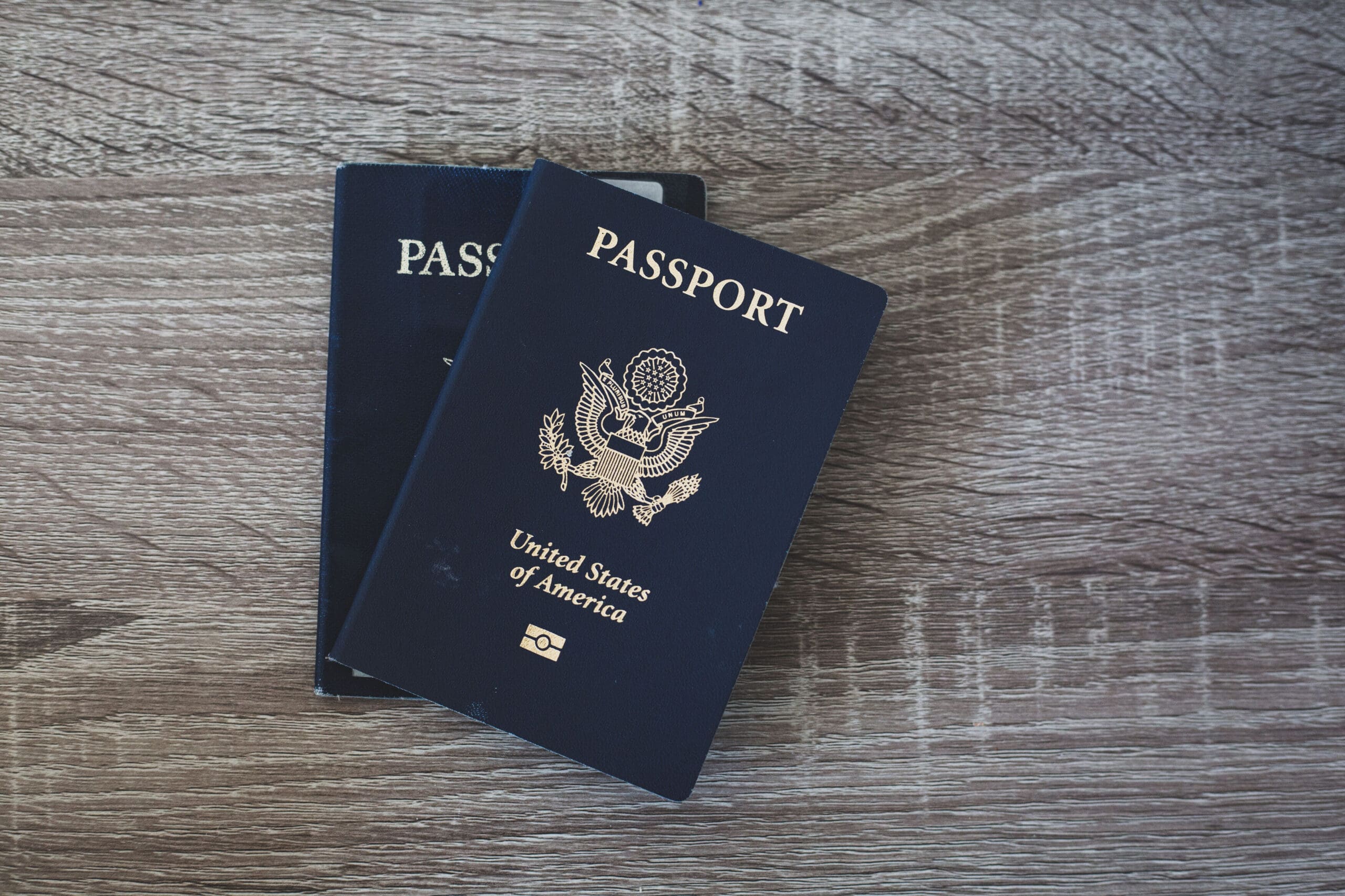 This image features two United States passports placed on a wooden surface, suggesting readiness for international travel. The dark blue covers of the passports contrast with the wood texture, evoking a sense of adventure and exploration.