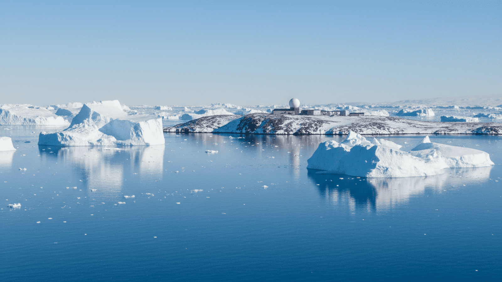 A vast Arctic landscape in Greenland featuring floating icebergs and a distant military radar station.