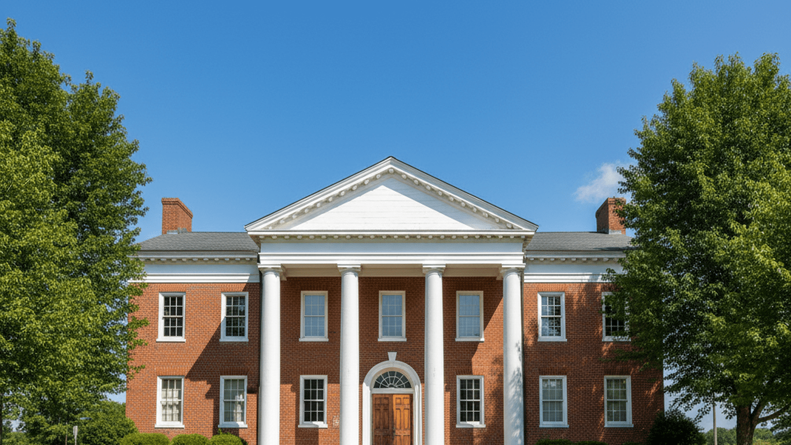 A quiet, stately brick courthouse with white columns stands under a clear sky.