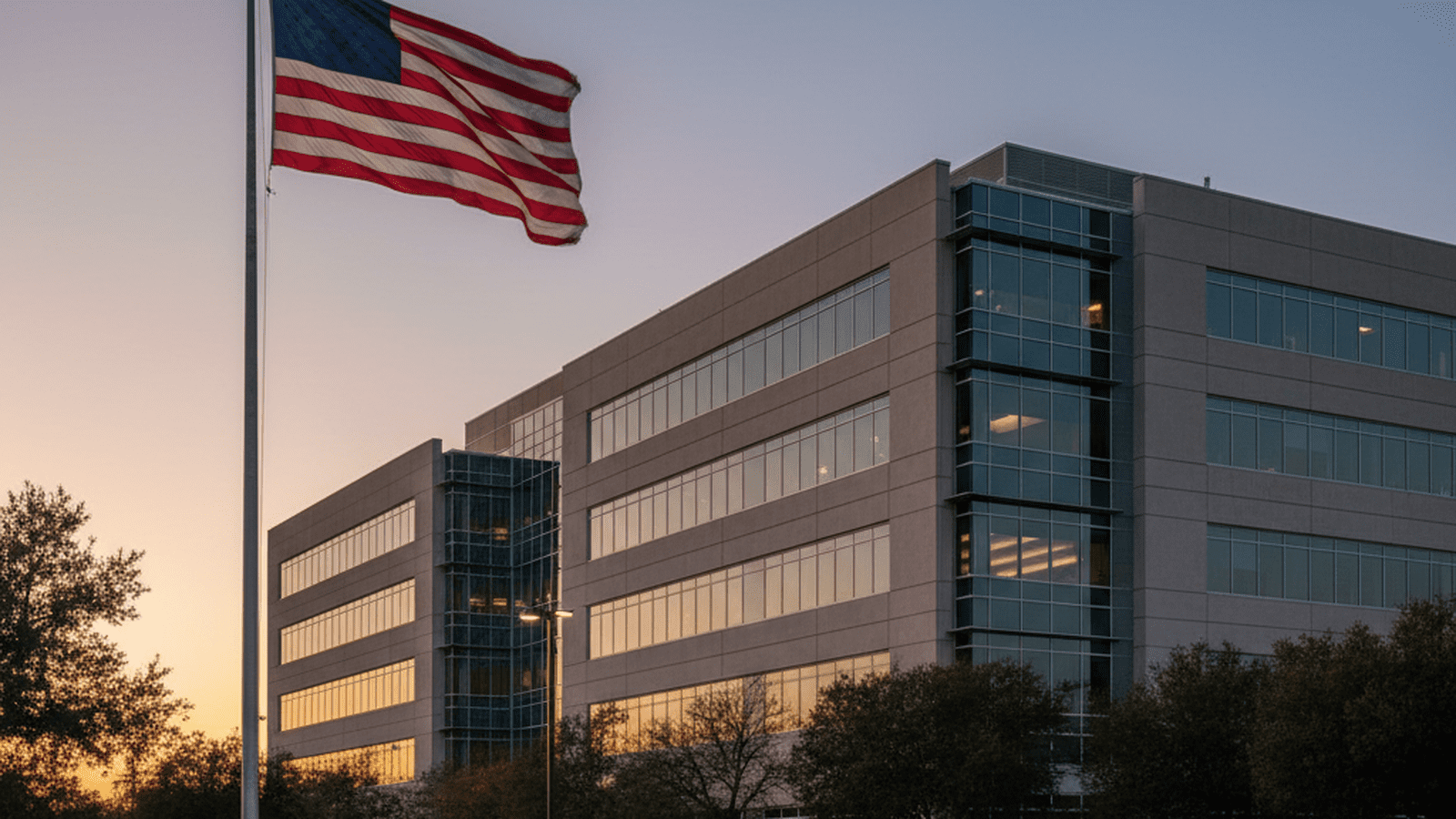 A fleet of white government vehicles parked in front of a federal building under a clear evening sky.