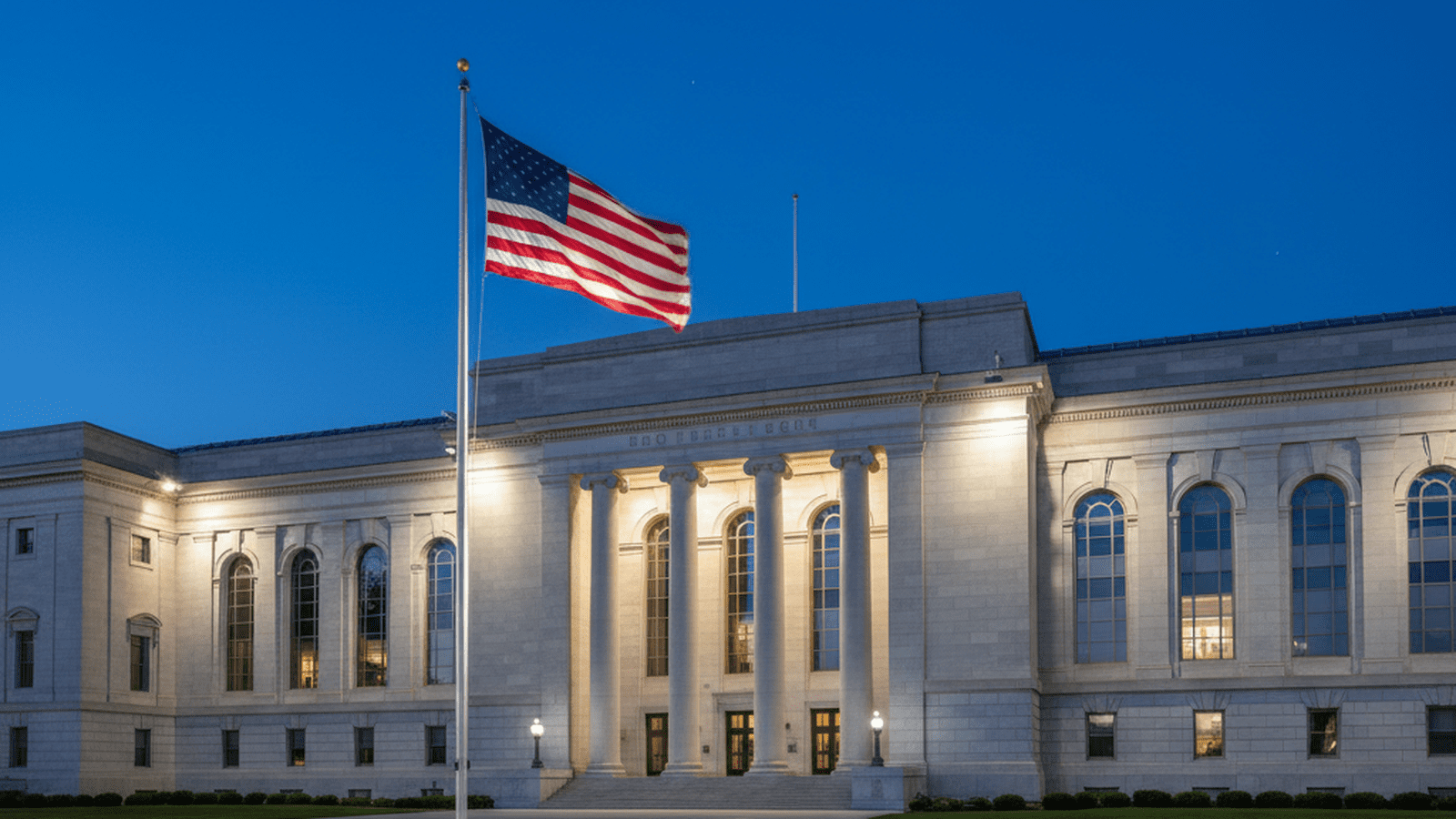 The Department of Homeland Security headquarters stands under a twilight sky with an American flag in the foreground.