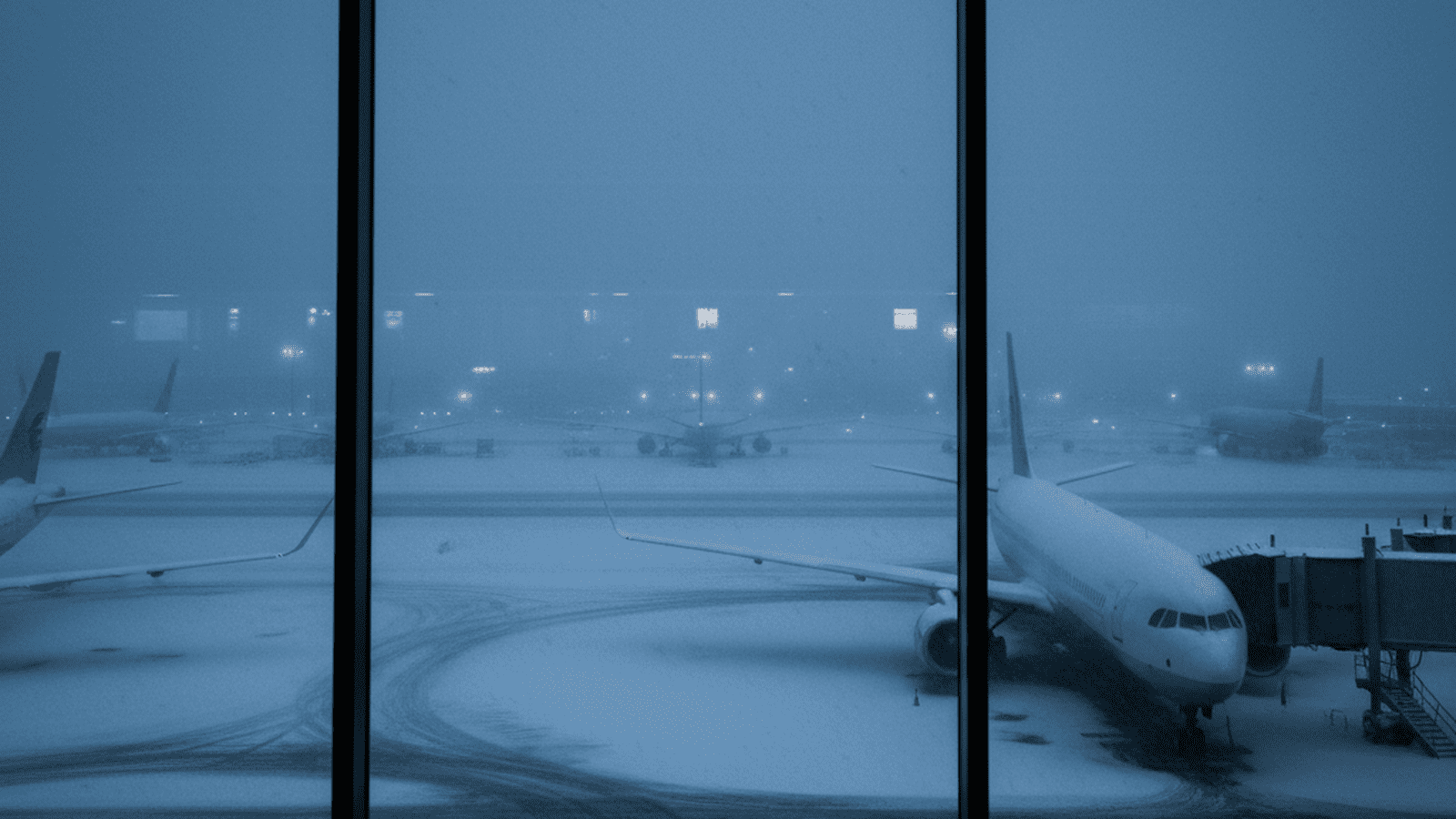 A quiet airport terminal overlooks a snowy runway with several grounded commercial airplanes parked at their gates.