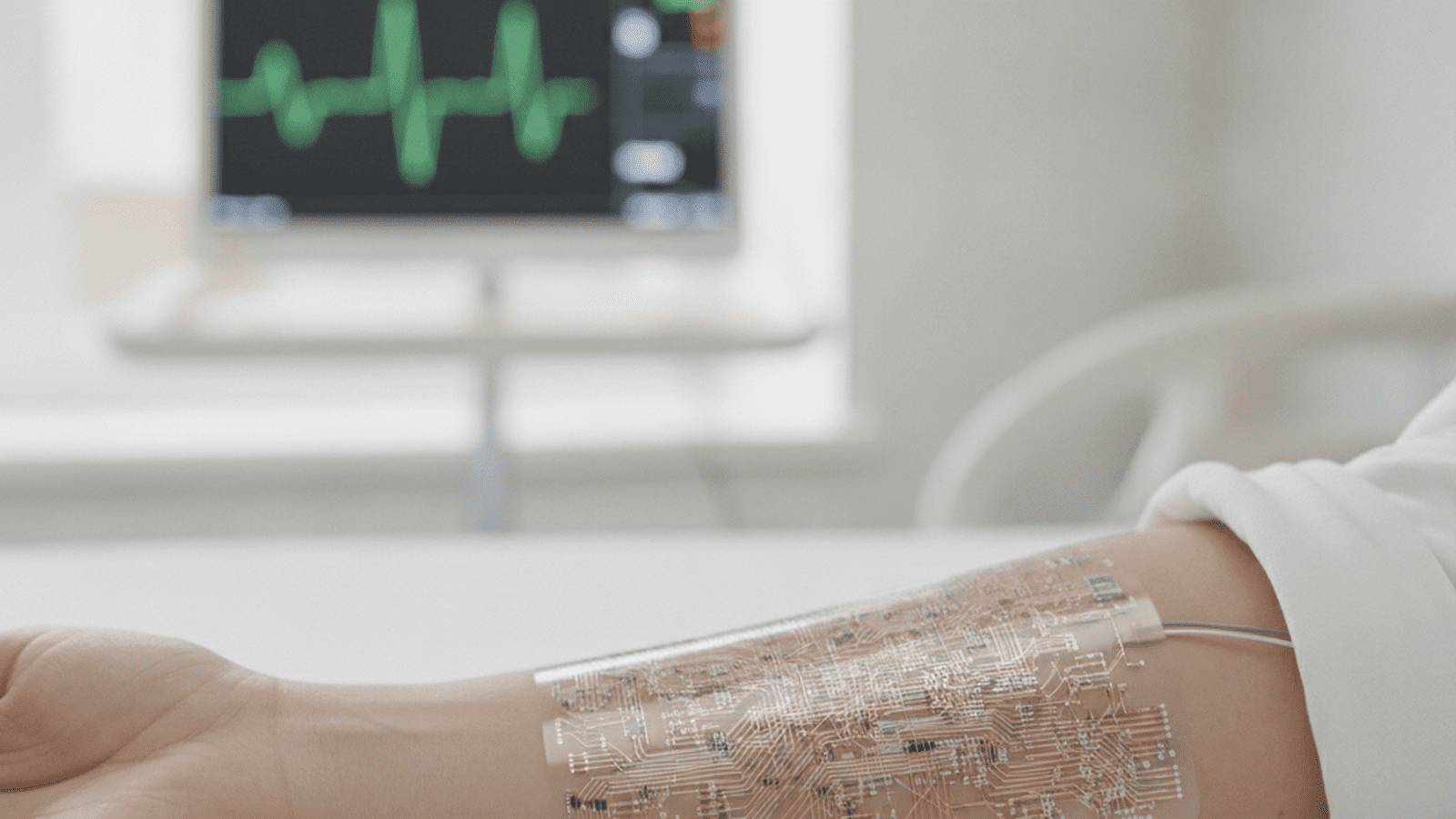 A flexible, transparent electronic sensor patch attached to a human arm in a clinical setting.