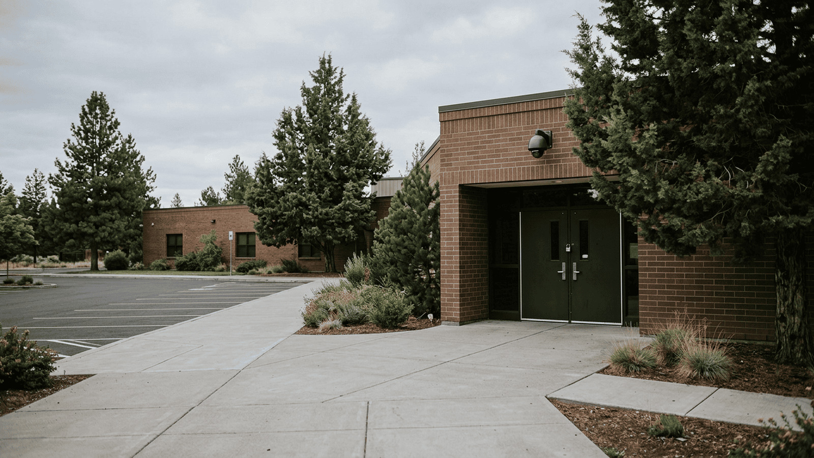 0e12e2692342dd5d6fbd7f7e2356aa18414944e23d8f10301e61a17e52dcee90 A quiet elementary school entrance with locked doors and a security camera.