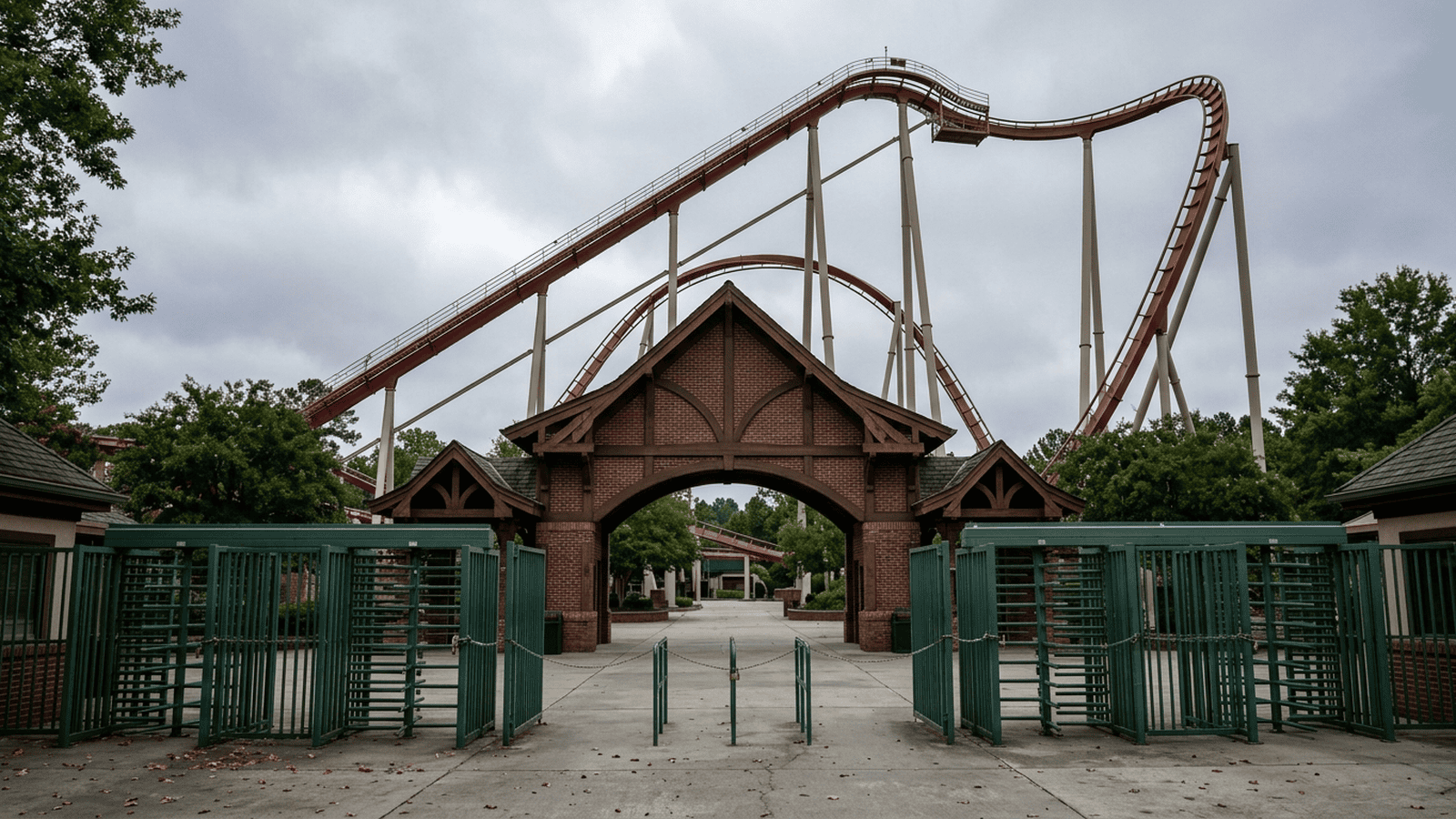 An empty roller coaster track rises above an amusement park entrance behind closed gates.
