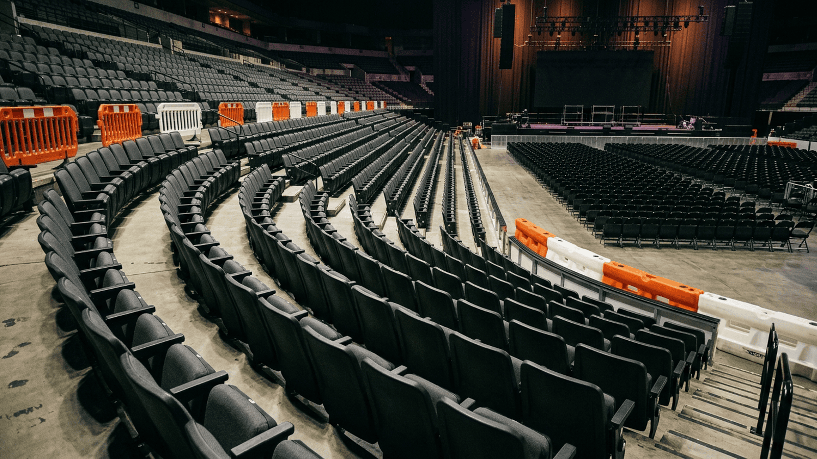 An indoor event venue with security barriers and a distant stage after a rally.