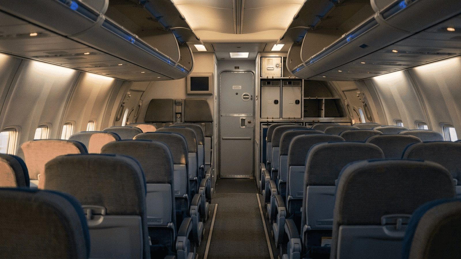 An empty airliner cabin faces a closed cockpit door with desert light coming through the windows.