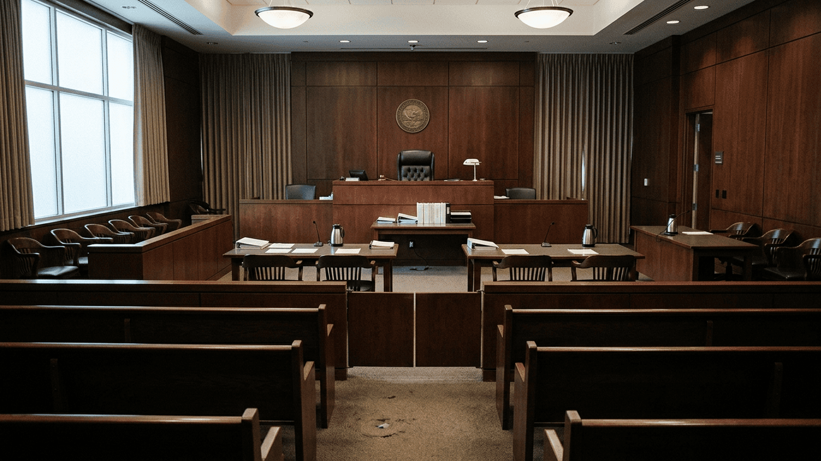 274355bd7d6fc51f6de6b04aa2b31f57815a4c75619588478c518f2415969fc4 An empty courtroom with a judge’s bench and counsel tables.