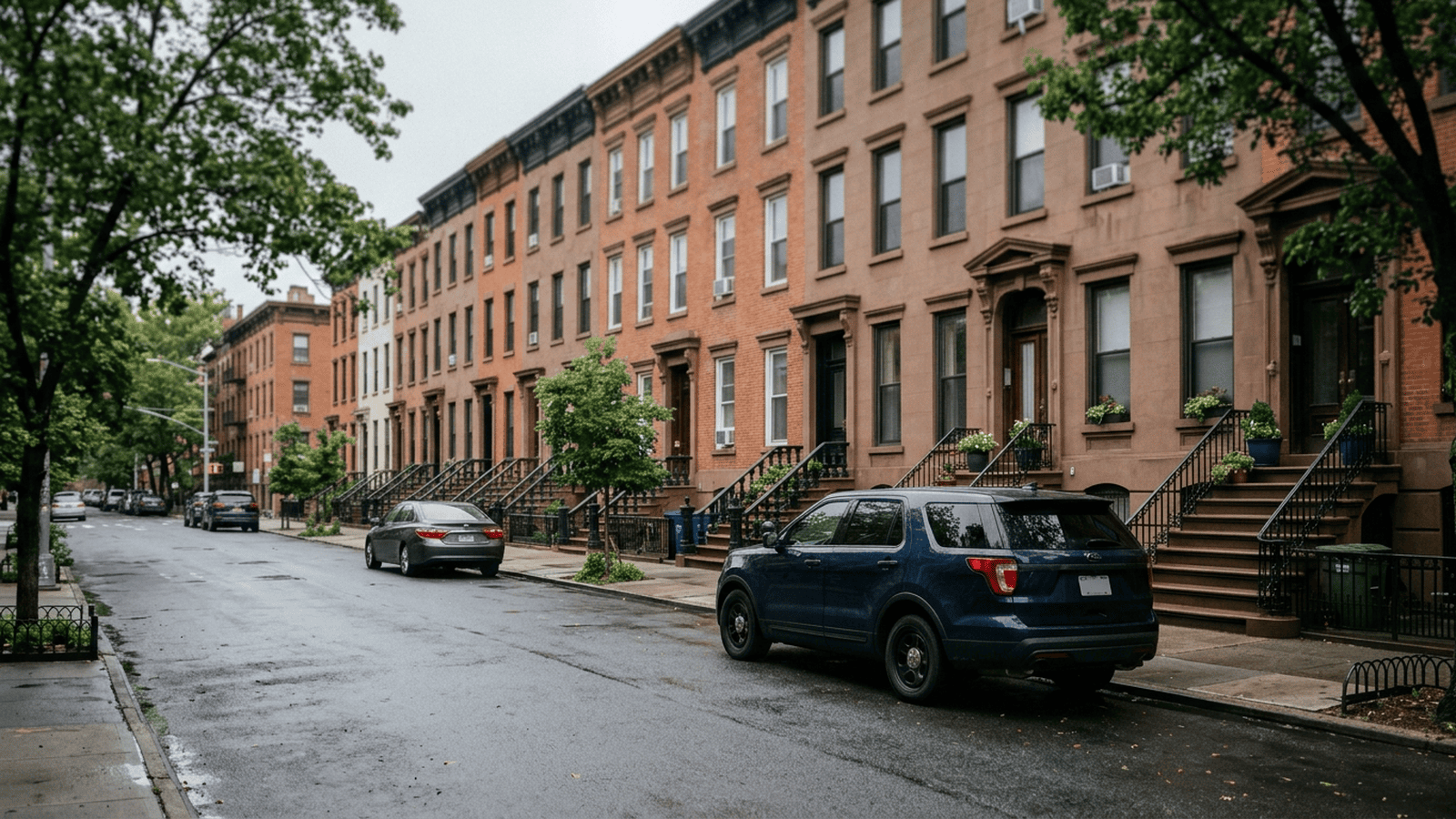 An unmarked vehicle sits on a quiet New York City residential street outside a townhouse.