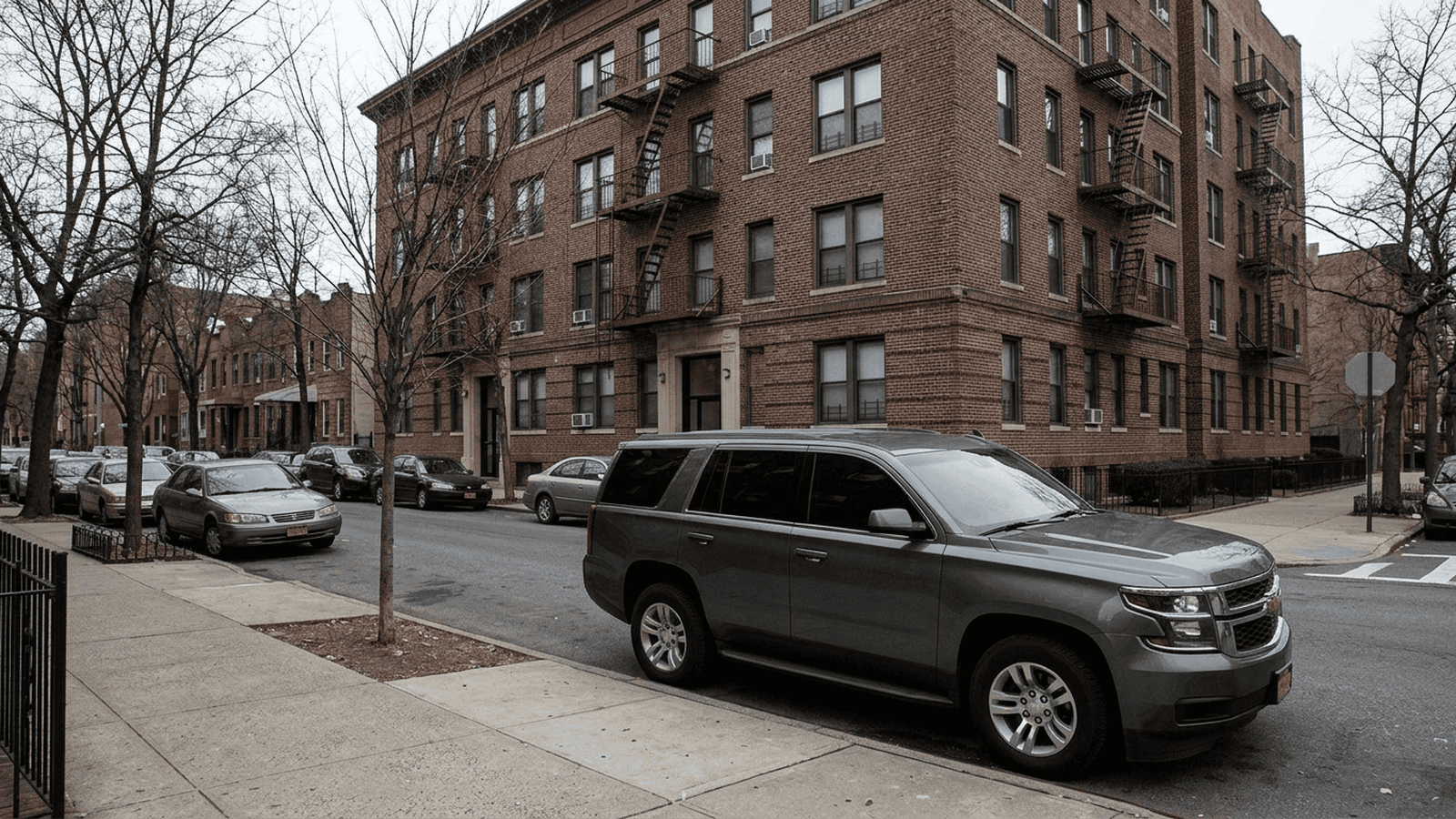 A quiet New York City residence and an unmarked vehicle on an overcast day.