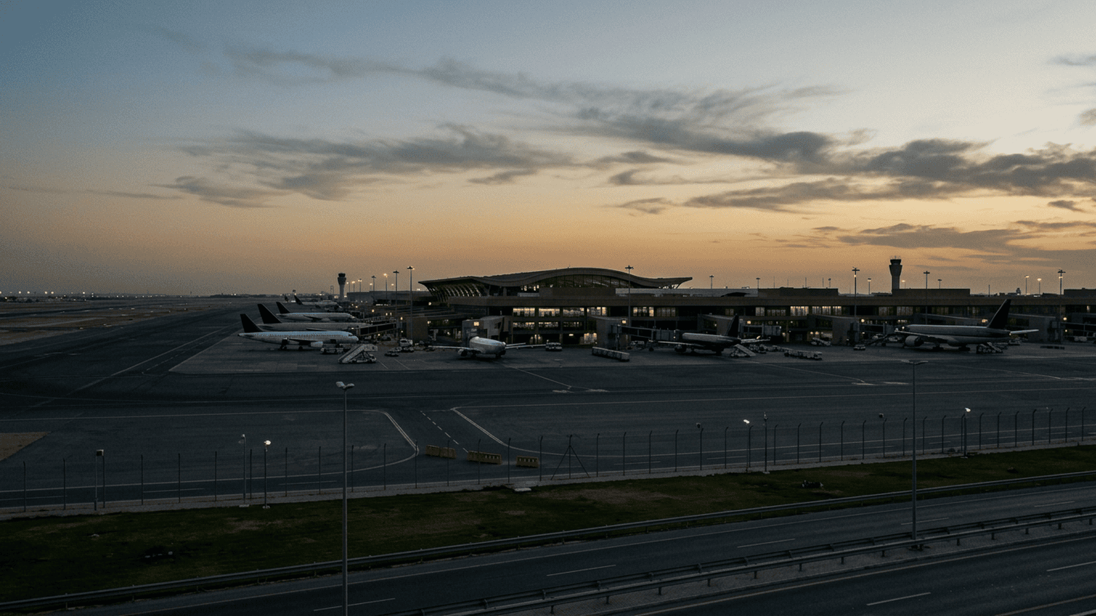 A distant view of an airport terminal and grounded aircraft at dusk.
