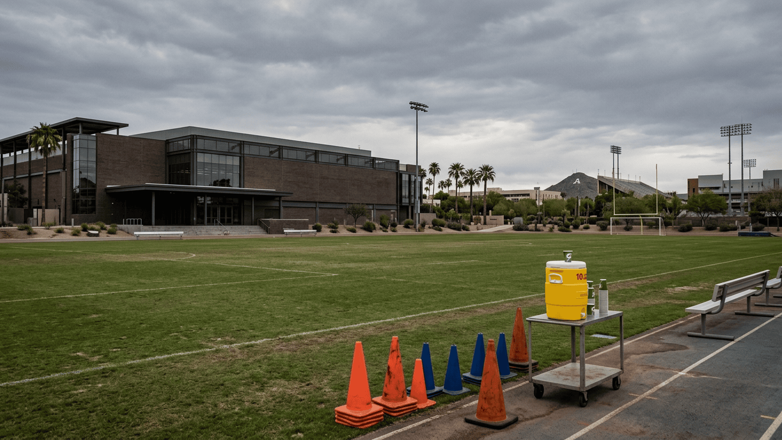 An empty athletic field with training cones and a water cooler beside a university hockey facility.
