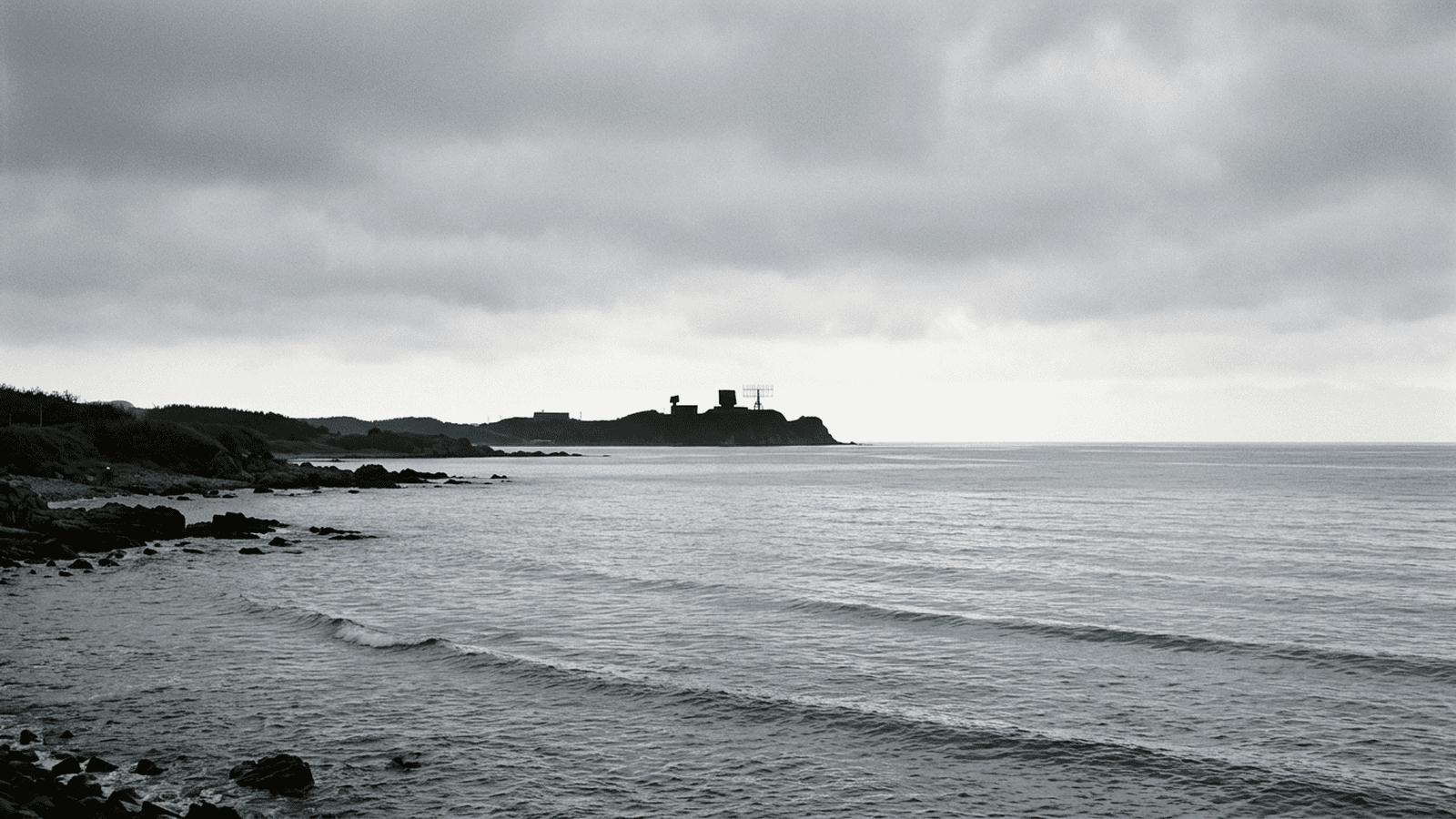 83e57c8d30737142b0e8735d709fd45bb4ecece1a26566ff314a6915b8c97ce4 A coastal radar installation overlooks a gray sea beneath an overcast sky.