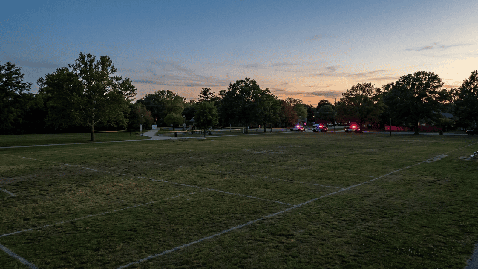 An empty park football field at dusk with police tape visible near the entrance.