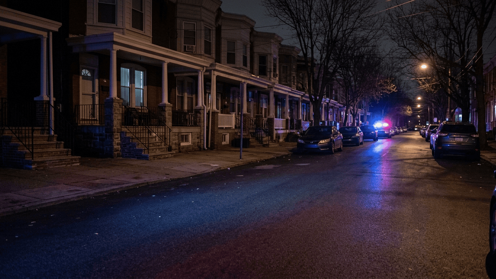Emergency lights reflect on a West Philadelphia residential street at night.